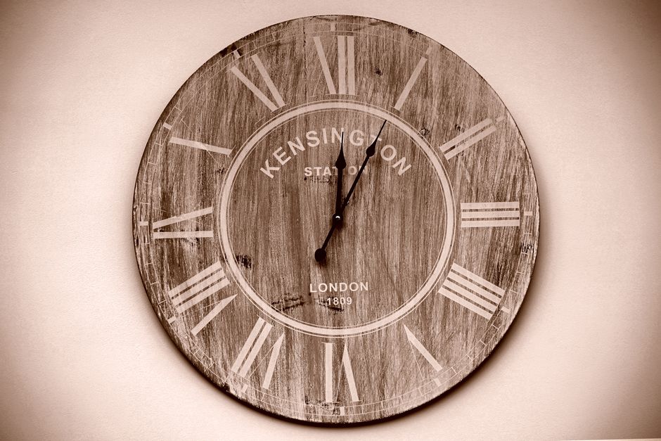 A close-up image of a round, analog wall clock featuring a white face with black Arabic numerals and black minute and hour hands, along with a thin black second hand. The clock shows the time as appro